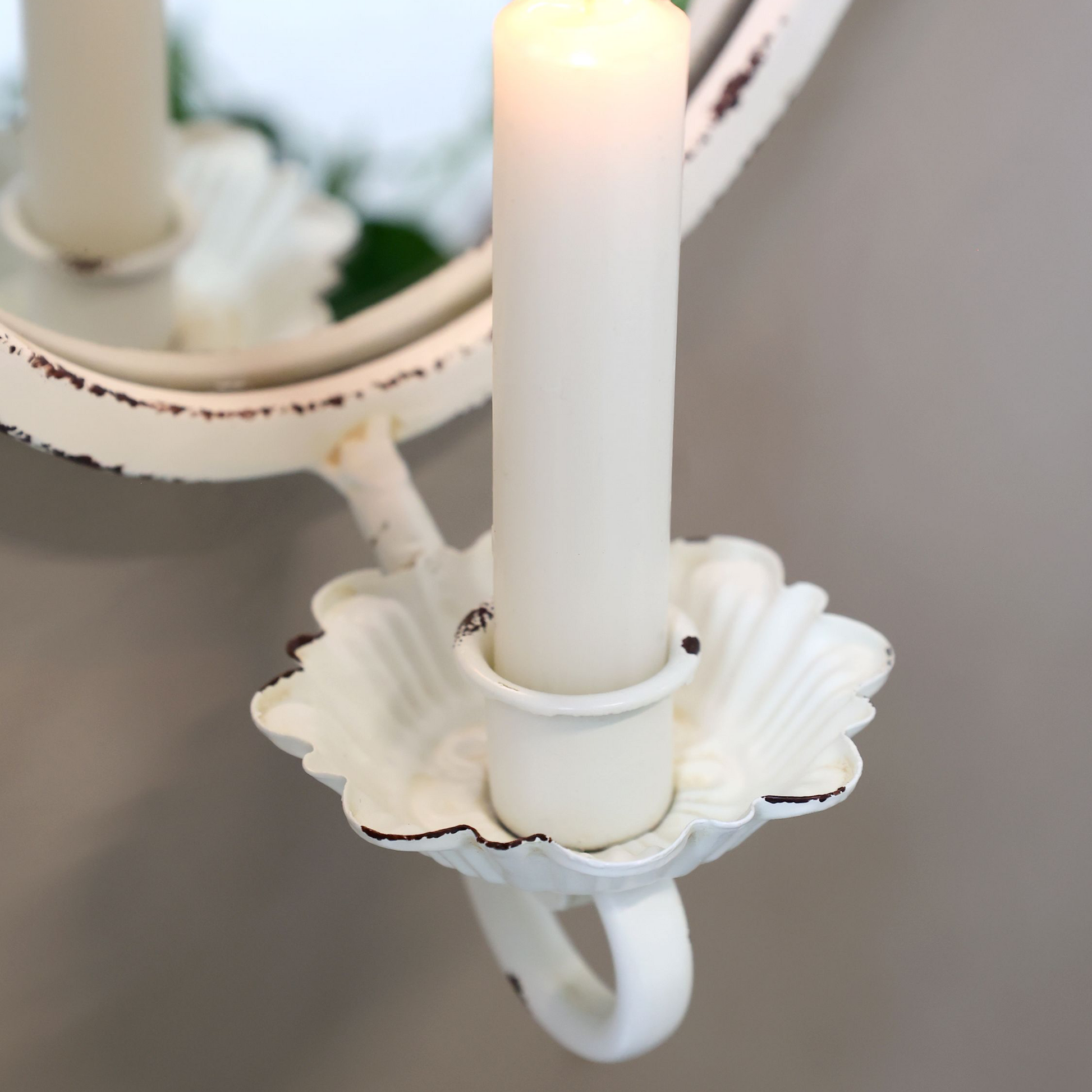White candle holder with a lit candle against a neutral background
