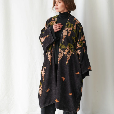 Woman wearing a dark floral-patterned coat against a white curtain background