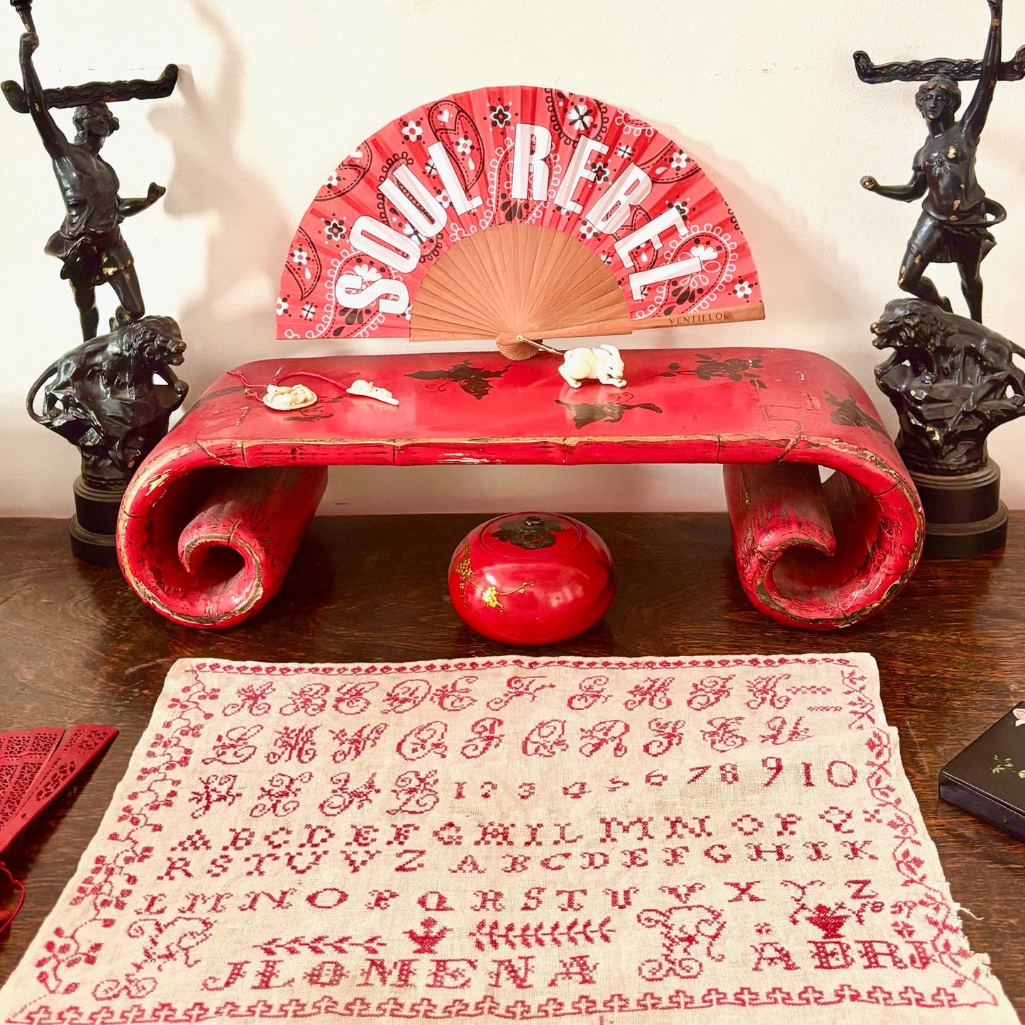 Red bench with decorative fan and patterned fabric on a wooden surface