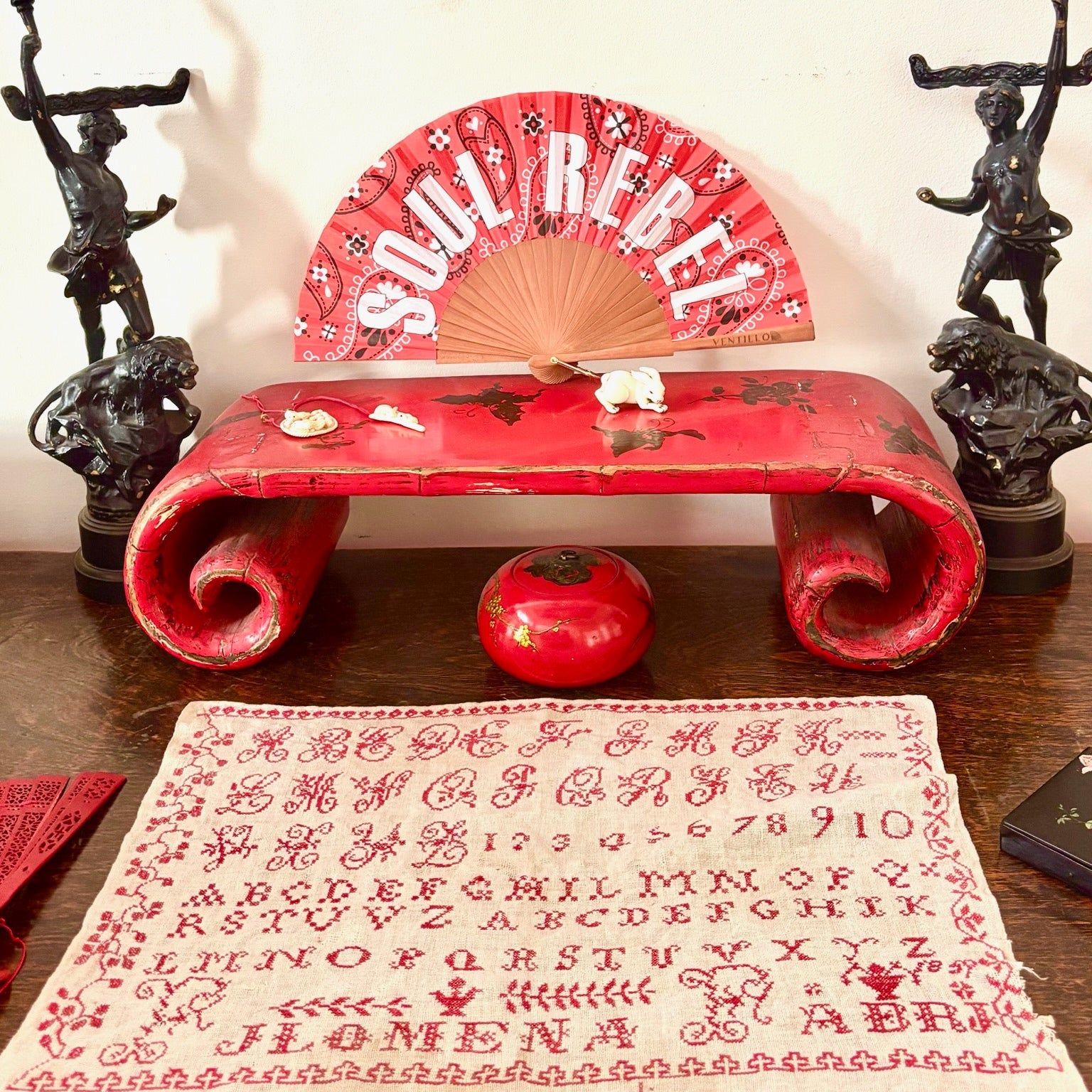 Red bench with decorative fan and patterned fabric on a wooden surface