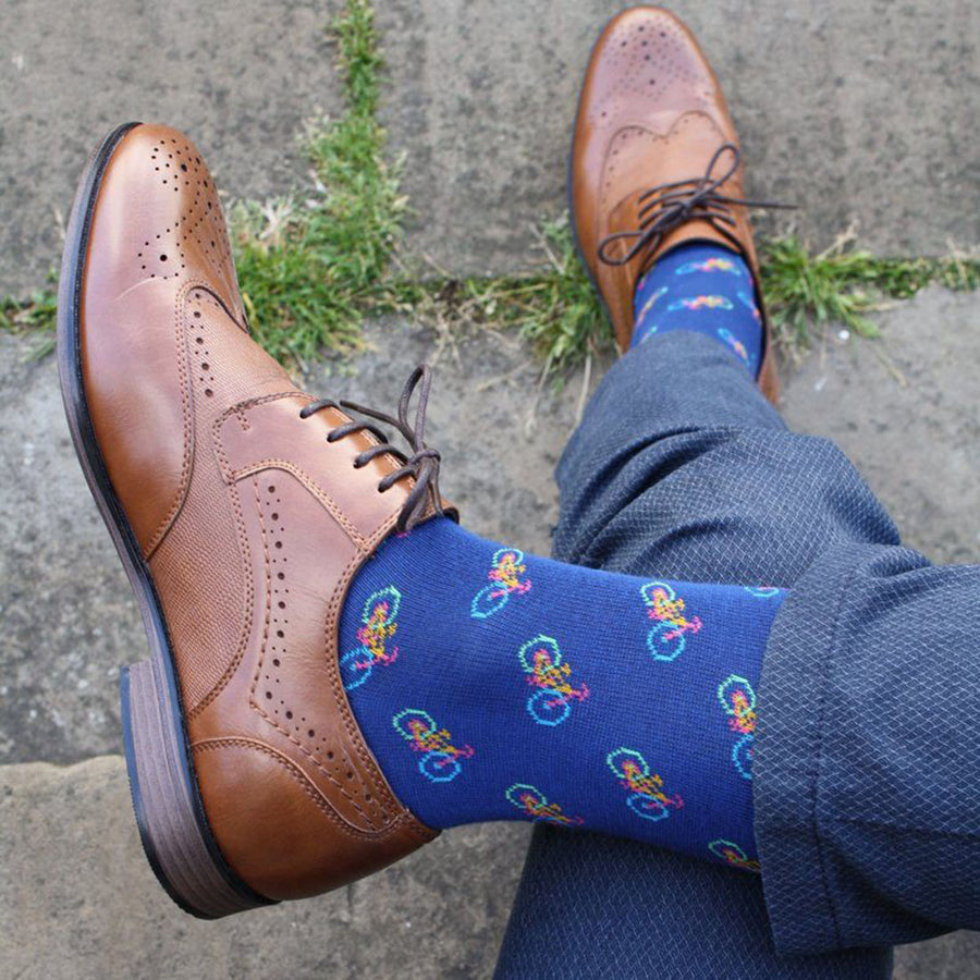 Brown dress shoes with blue socks featuring colorful patterns on a concrete surface.