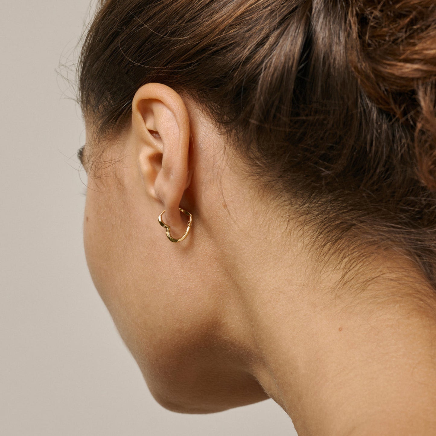 Close-up of a person wearing a gold hoop earring on a neutral background