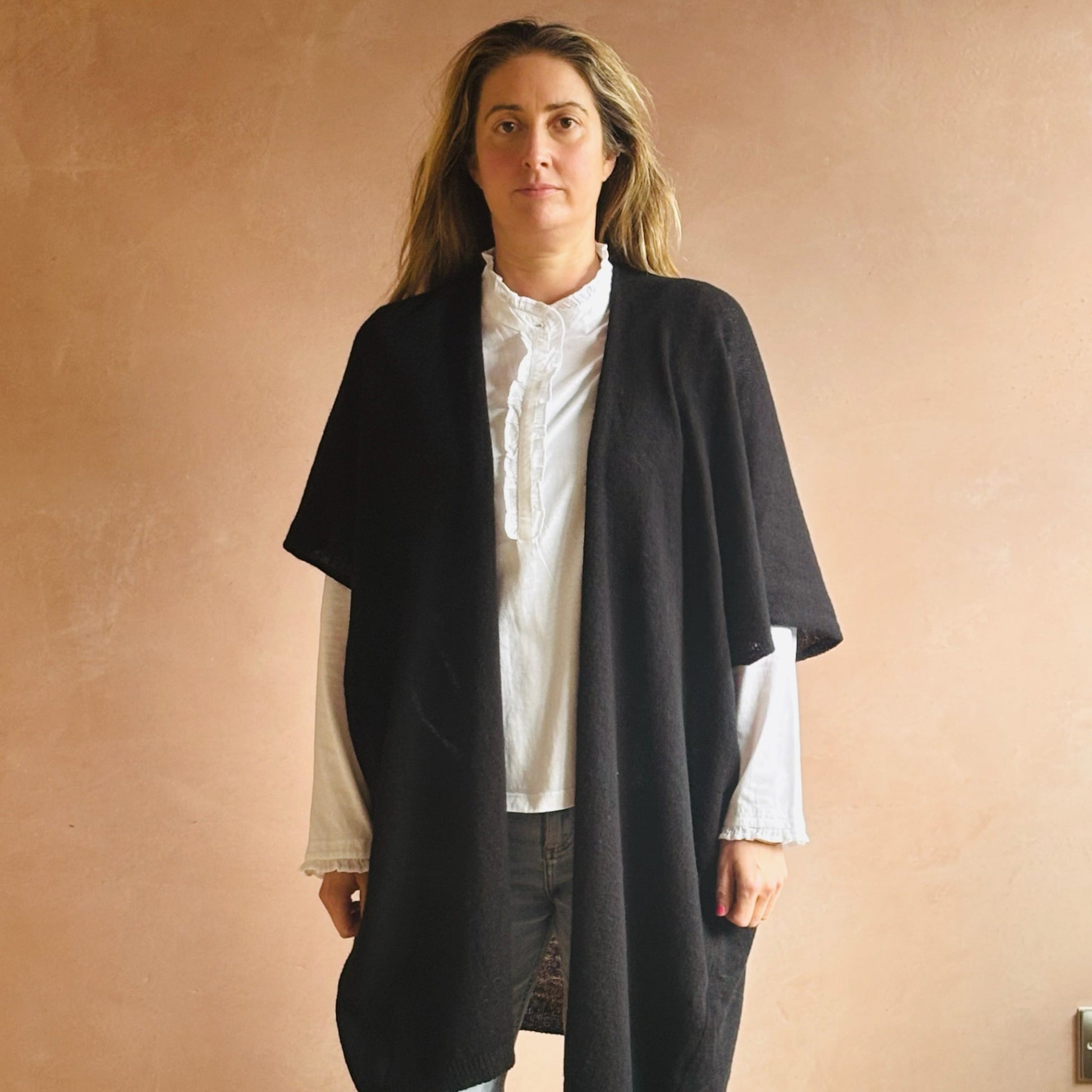 Woman wearing a black sleeveless cardigan over a white shirt against a beige wall