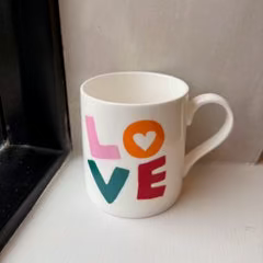 White mug with colorful 'LOVE' design on a white surface.