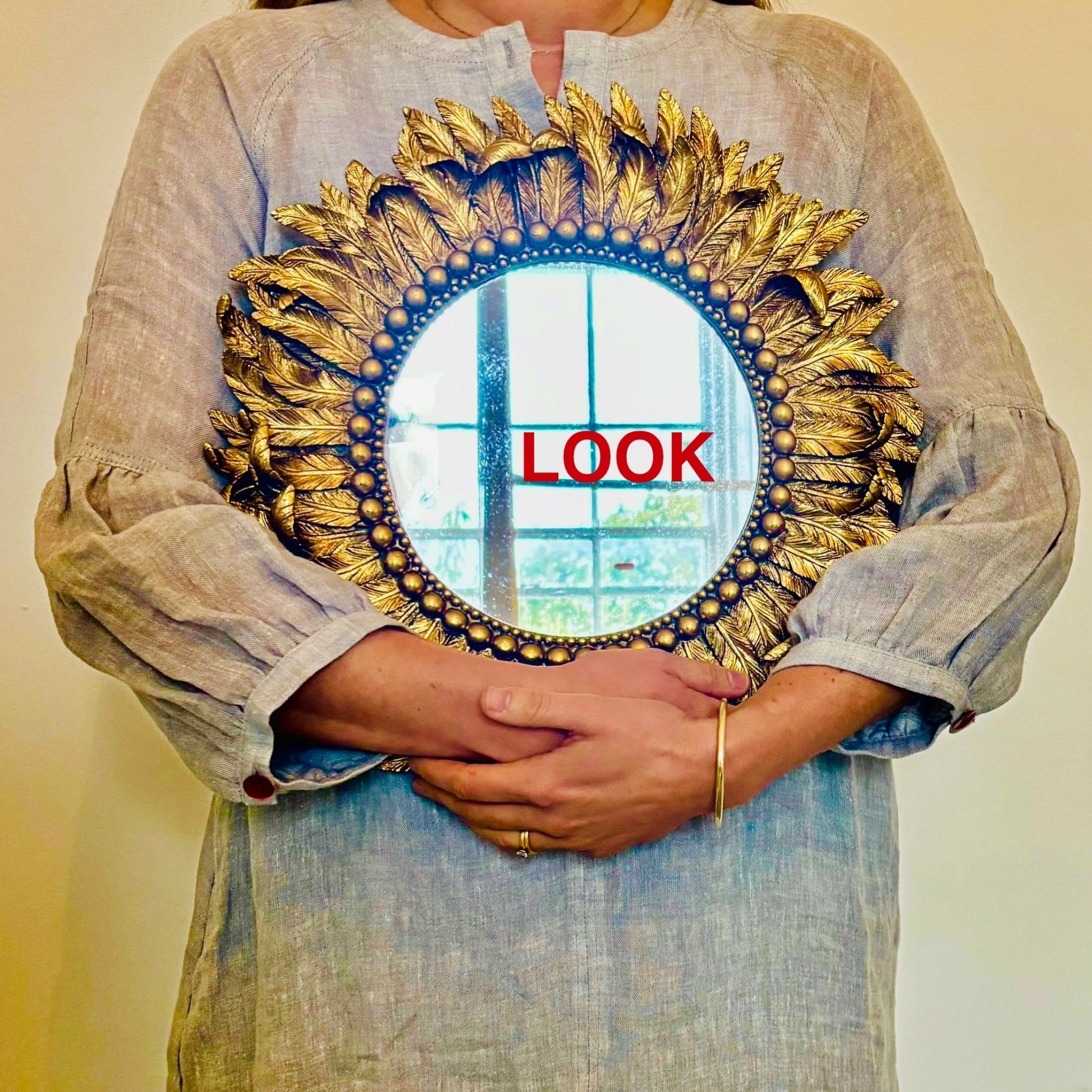 Person holding a decorative mirror with a 'LOOK' text overlay