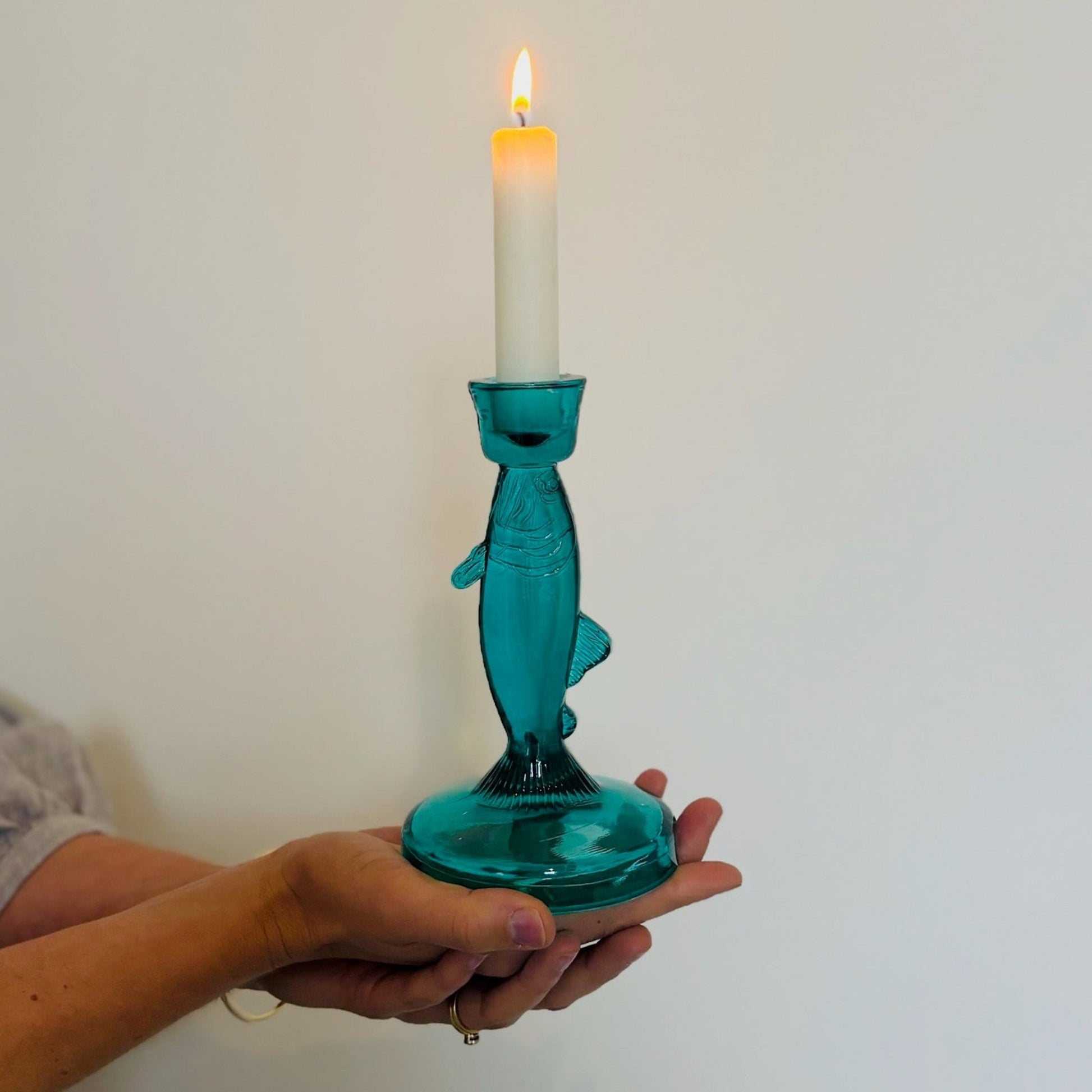 Teal glass candle holder with a lit candle against a plain background