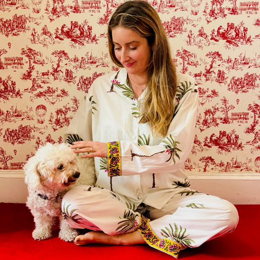 Woman in a floral robe petting a small dog against a decorative red and white wallpapered wall.