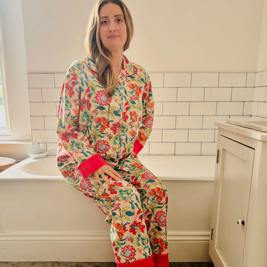 Woman wearing colorful floral pajamas sitting on a bathtub edge in a bathroom.