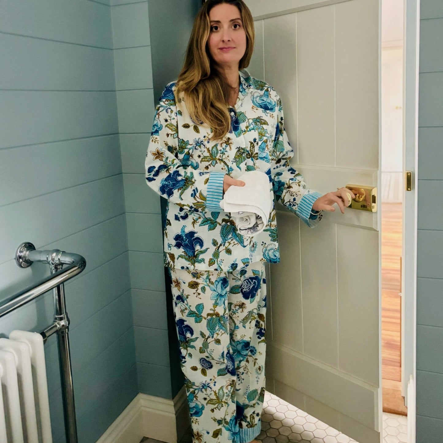 Woman in floral pajamas standing in a bathroom.