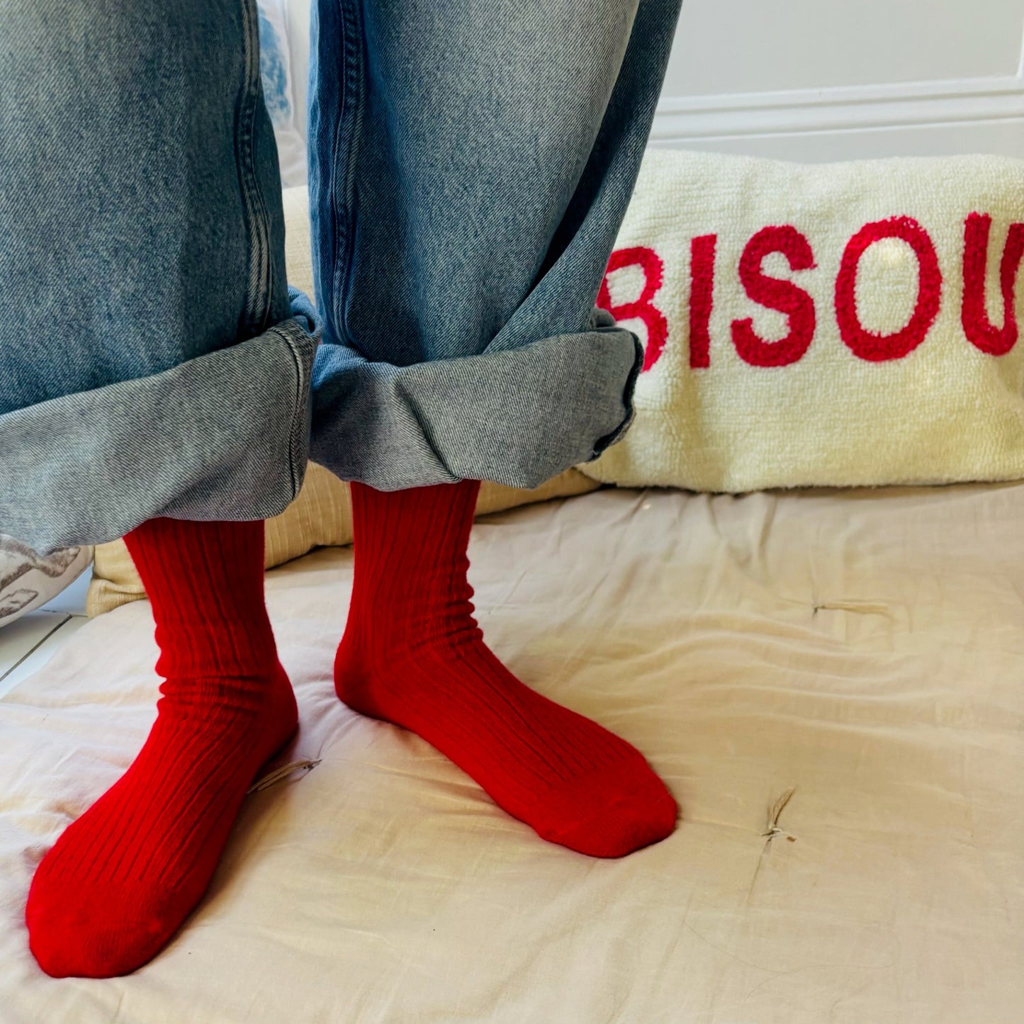 Person wearing red socks with blue jeans on a beige surface, with 'BISOU' text in the background.