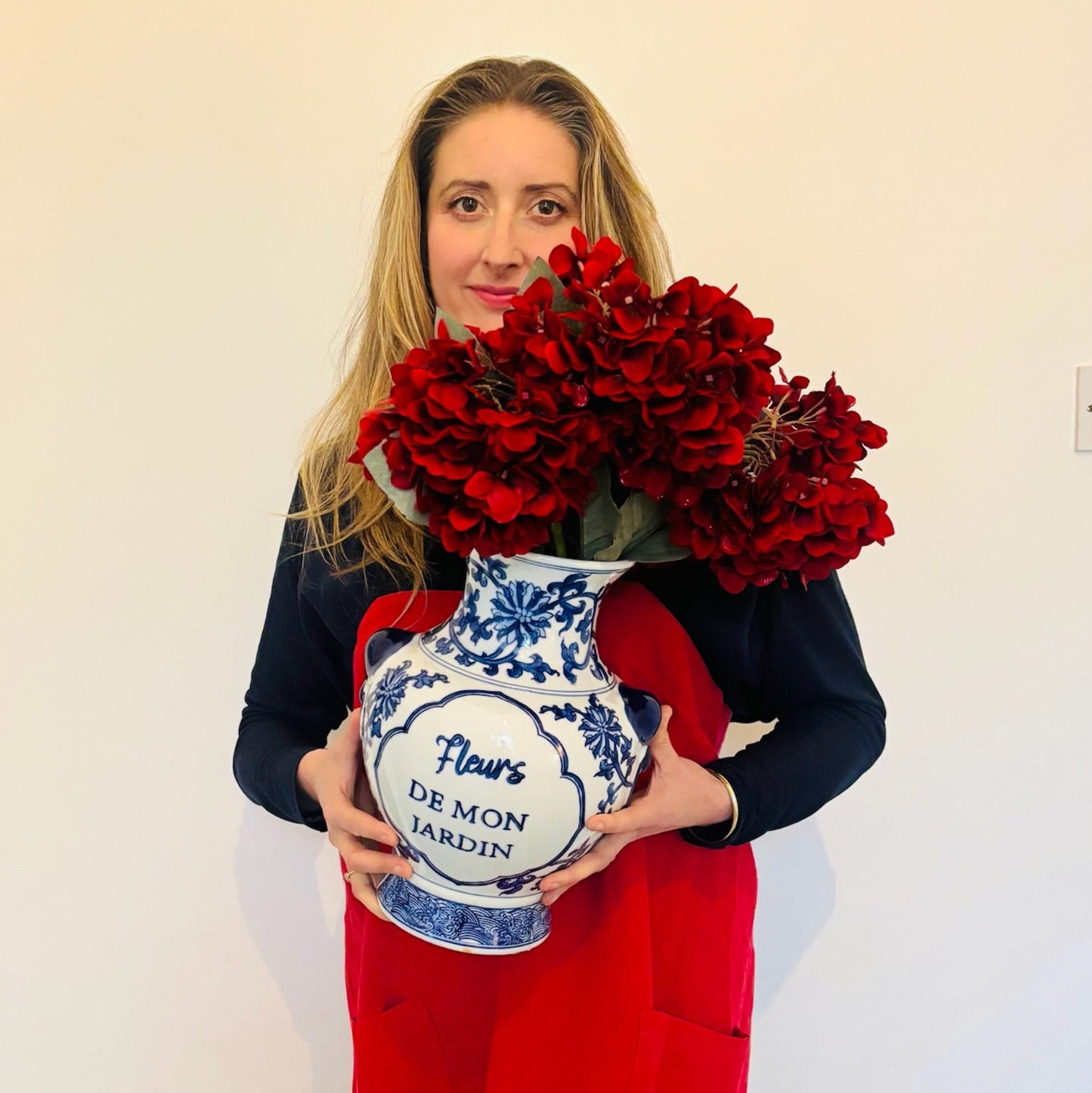 Woman holding a bouquet of red flowers and a decorative vase with a white background
