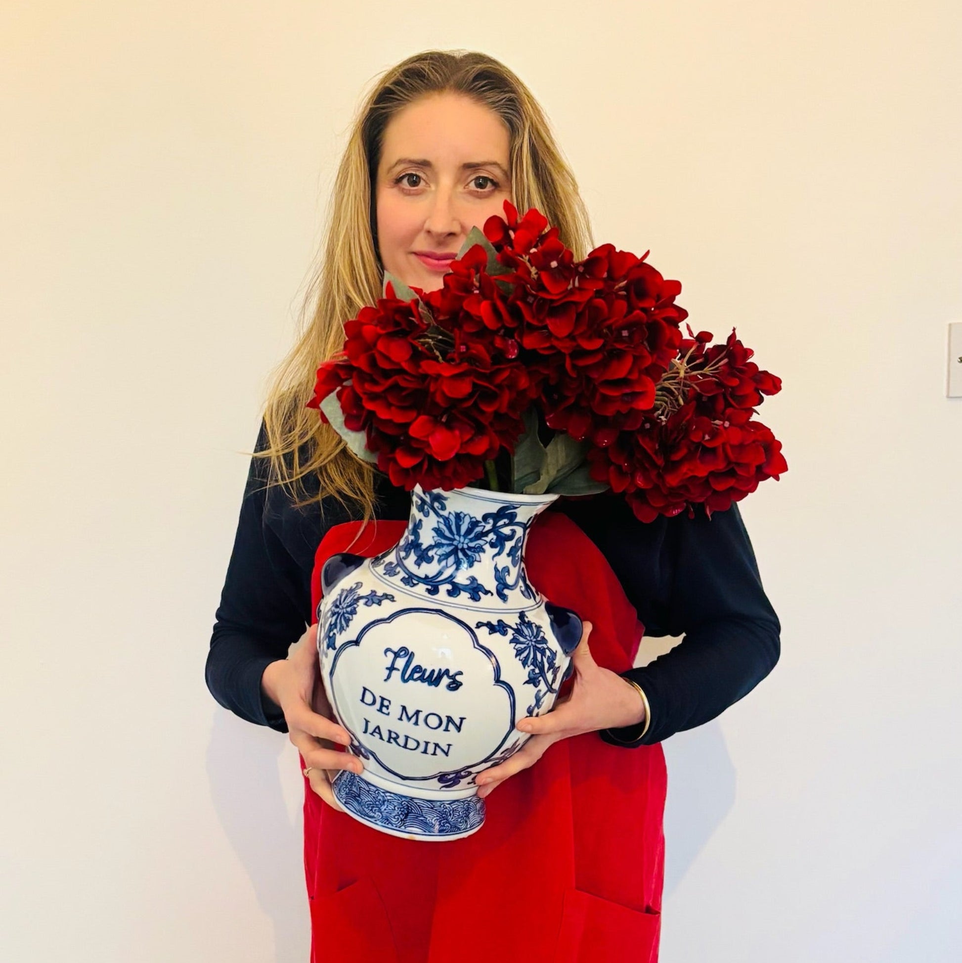 Woman holding a bouquet of red flowers and a decorative vase with a white background