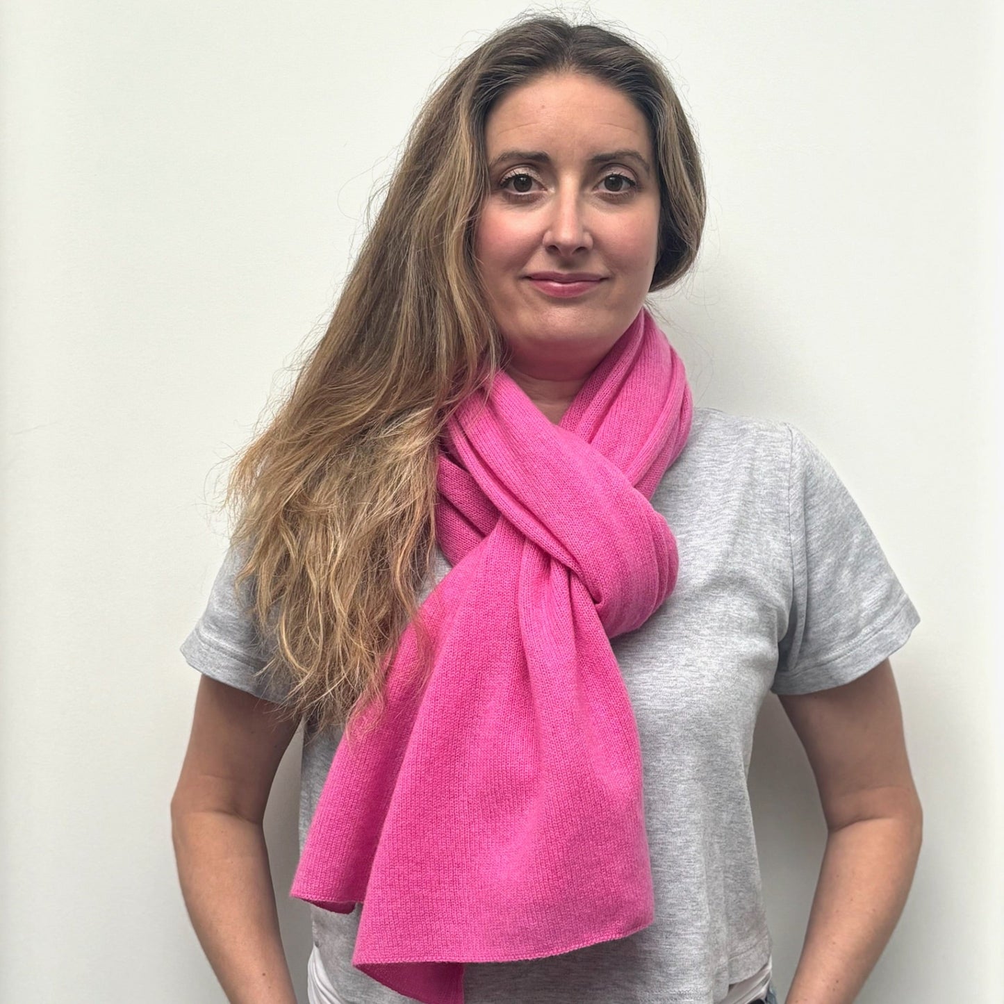 Woman wearing a bright pink scarf and gray shirt against a white background