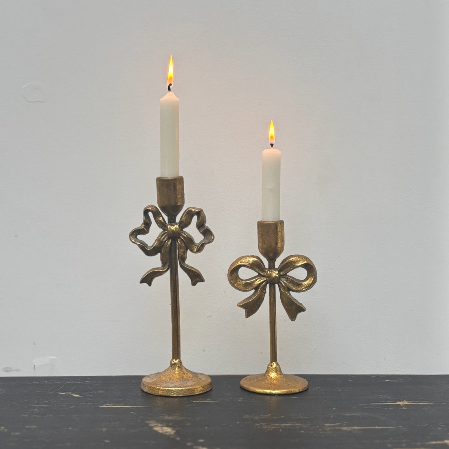 Two gold candle holders with candles on a dark surface and light gray background