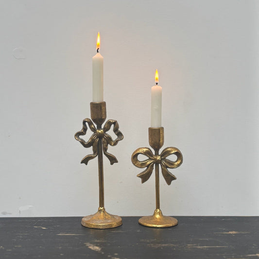 Two gold candle holders with candles on a dark surface and light gray background