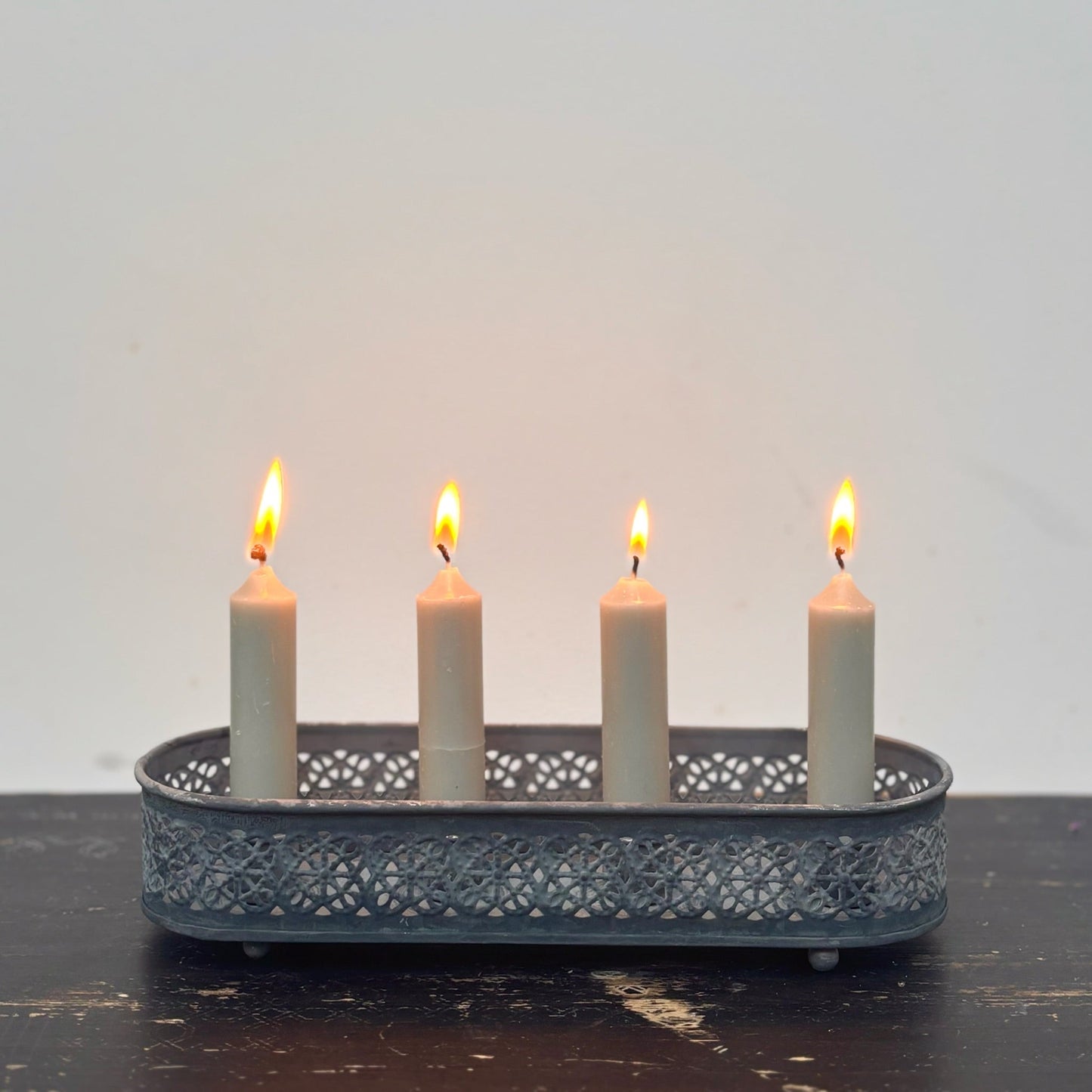 Candle holder with four lit candles on a dark surface and light gray background