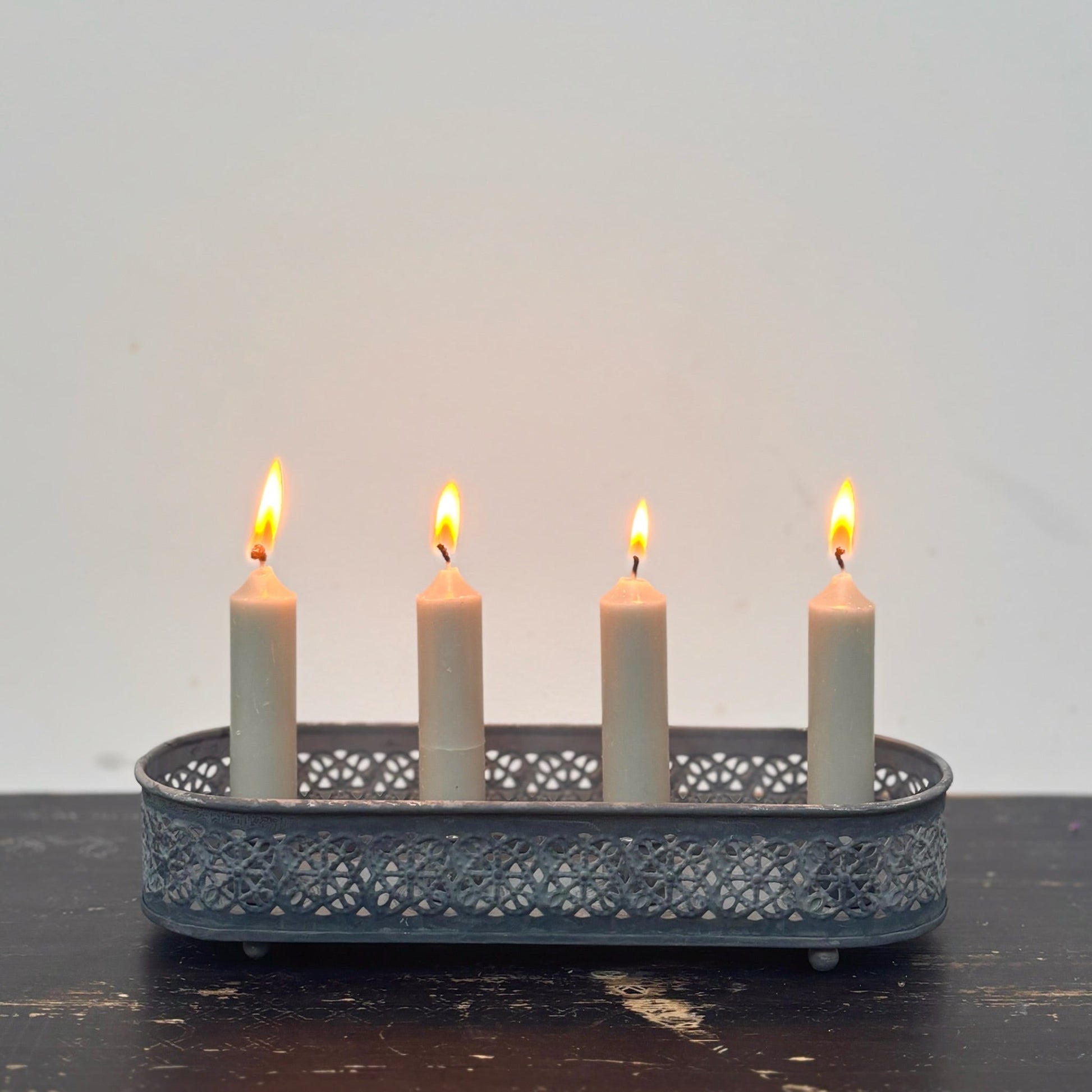 Candle holder with four lit candles on a dark surface and light gray background