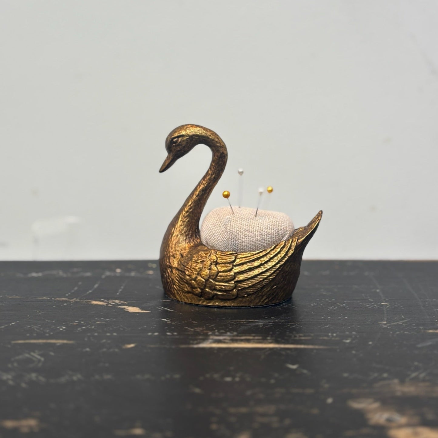 Gold swan-shaped pincushion on a dark surface with a light gray background