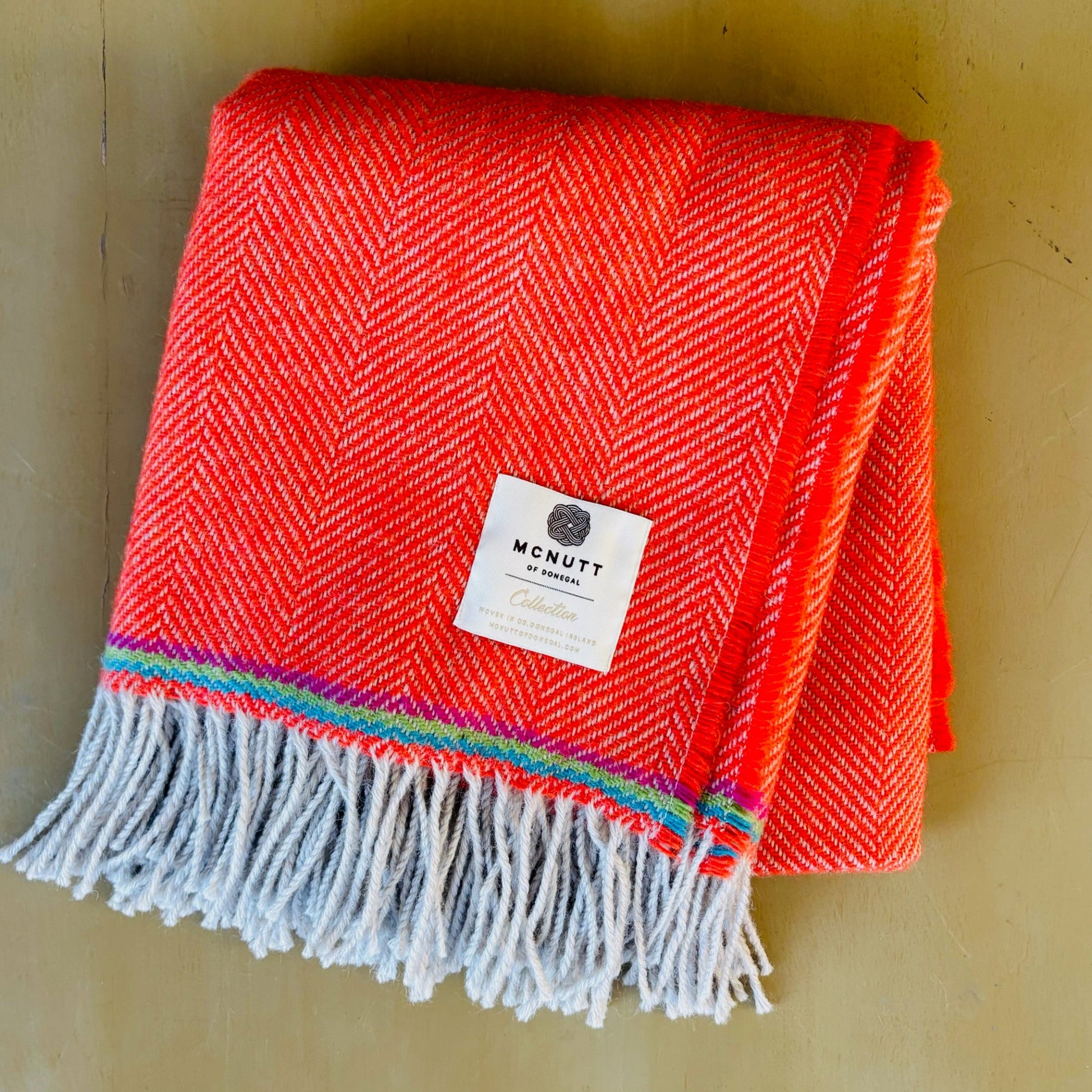 Red woven blanket with colorful fringe and a label on a wooden surface