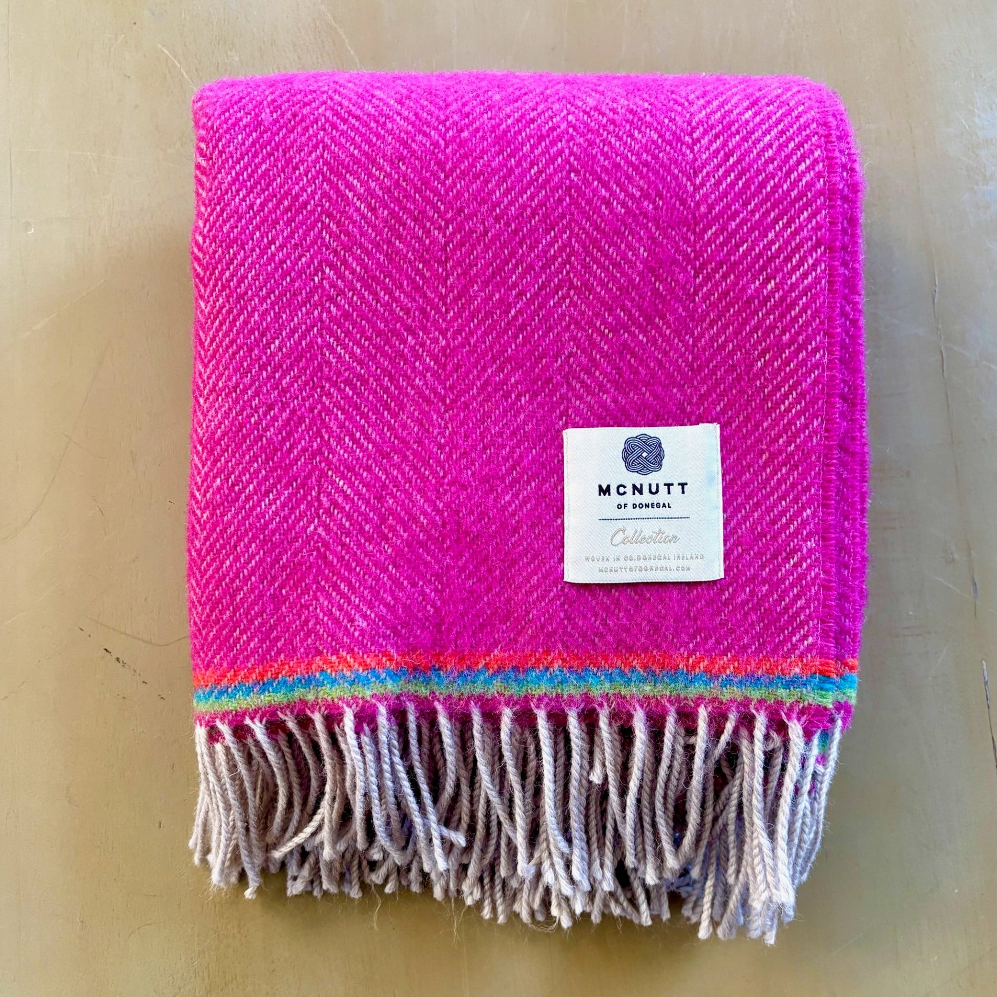 Pink woven blanket with fringes and a visible brand label on a beige background