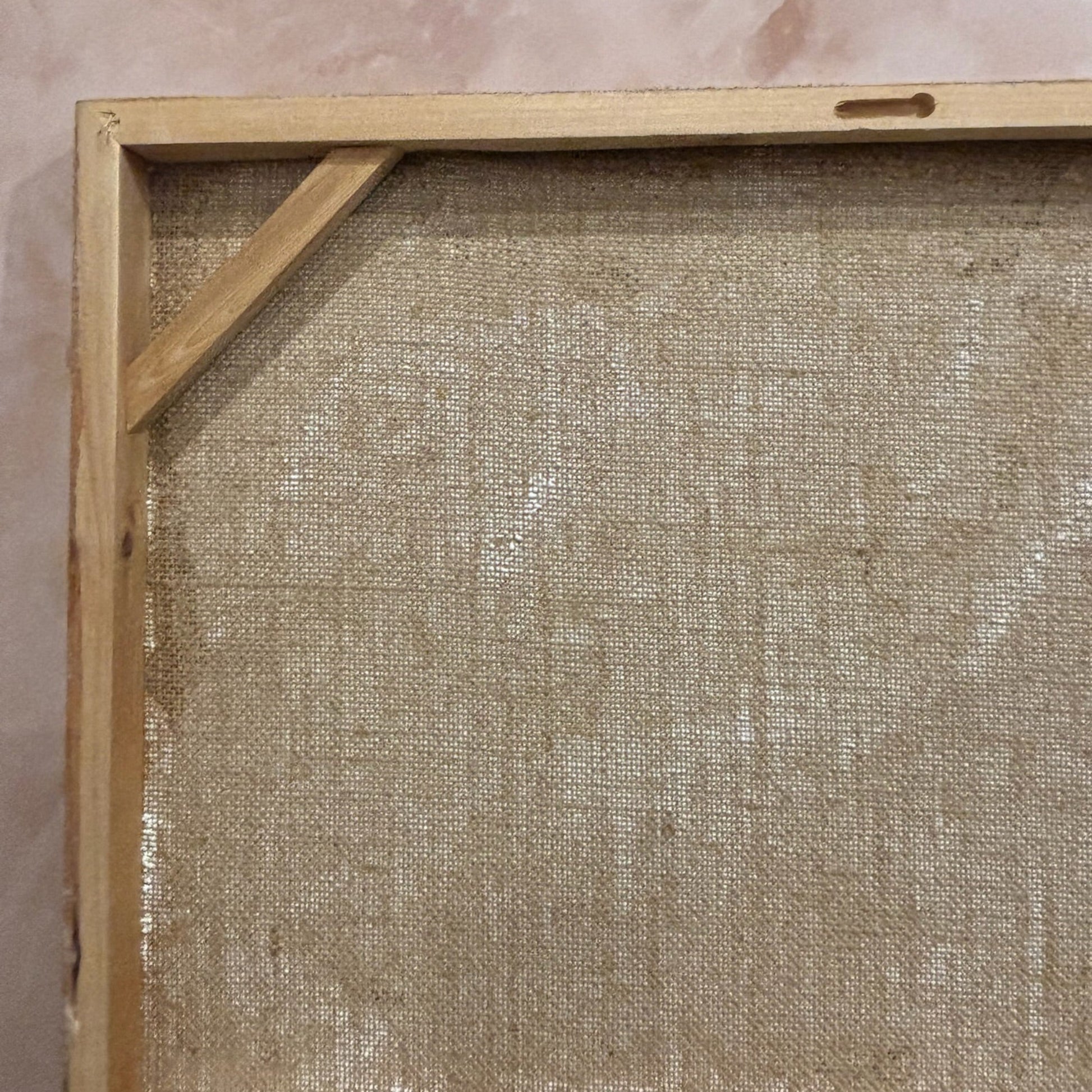 Wooden picture frame with a textured beige mat against a pinkish-brown wall.