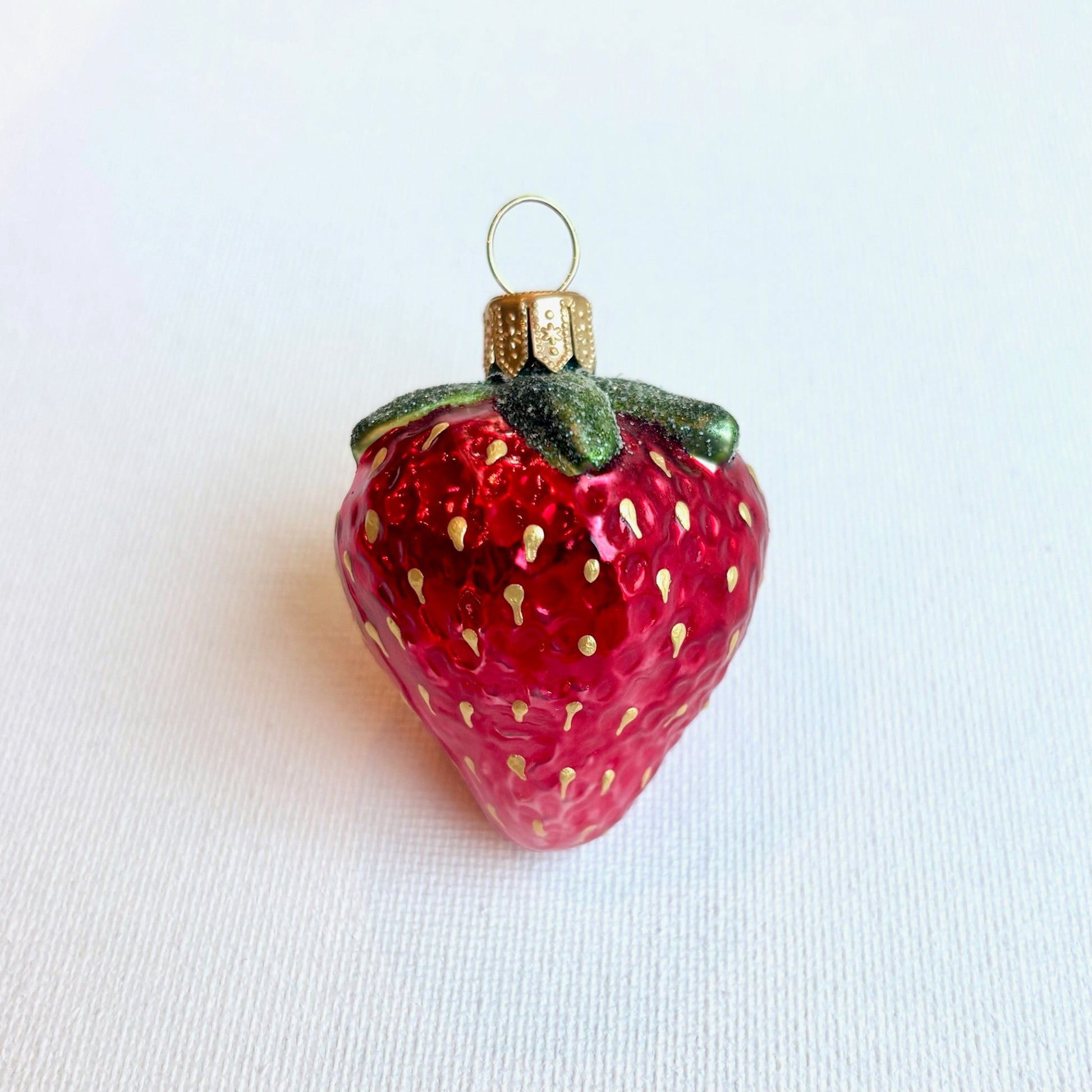 Strawberry-shaped ornament with gold seeds on a white background