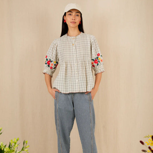 Woman wearing a checkered shirt with floral sleeves and blue pants against a beige background