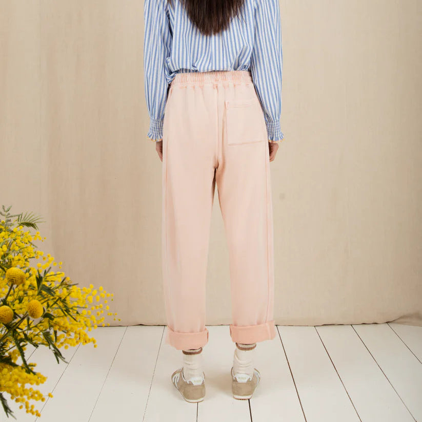 Person wearing a blue striped shirt and pink pants standing against a beige wall with a white floor.