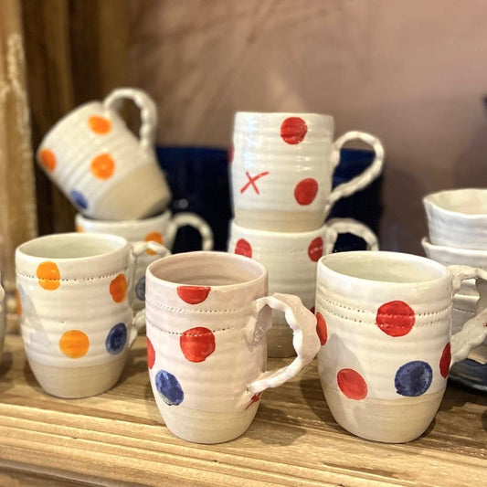 Handmade Irish ceramic mugs with colorful polka dots on a wooden surface.
