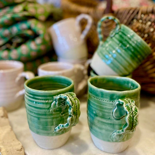 Two green ceramic mugs with handles on a table with blurred background