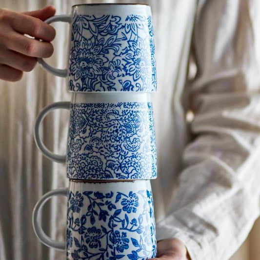 Stack of blue and white patterned ceramic mugs held by a person against a neutral background