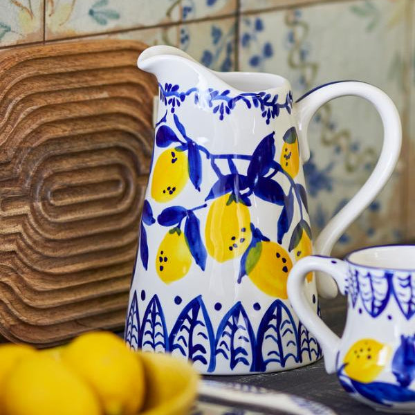Ceramic pitcher and mug with lemon design on a wooden surface and tiled wall background